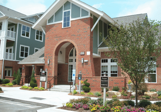 Brick apartment building entrance with landscaped walkway and signage
