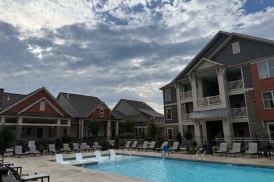 Apartment complex pool with lounge chairs under cloudy sky
